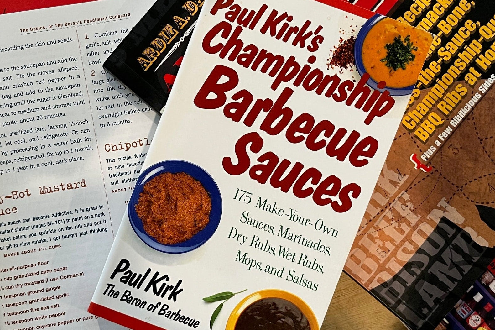 Book titled 'Paul Kirk's Championship Barbecue Sauces' on a table with other books.