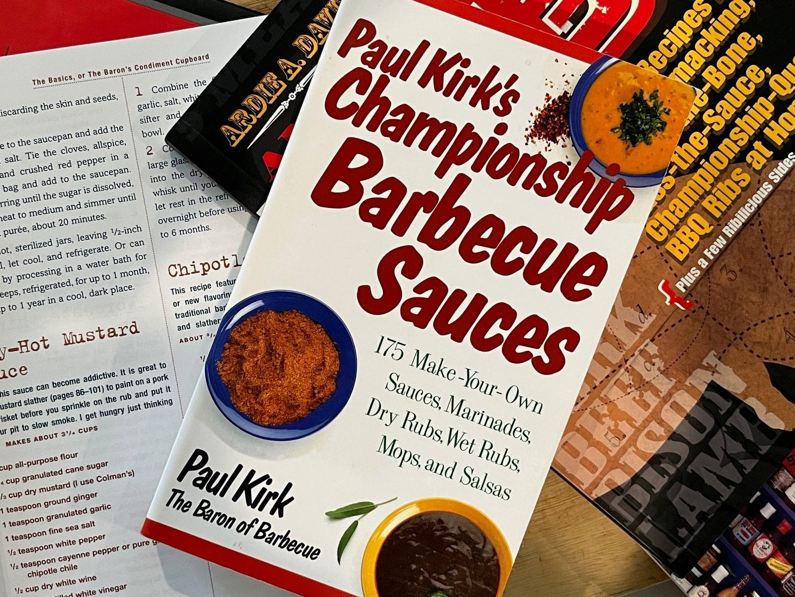 Book titled 'Paul Kirk's Championship Barbecue Sauces' on a table with other books.