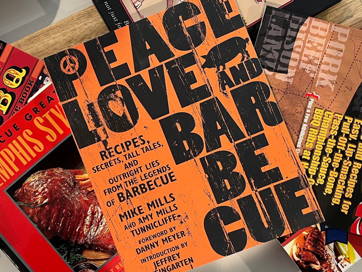 Collection of cookbooks on a wooden surface with 'Peace Love and Barbecue' prominently displayed.